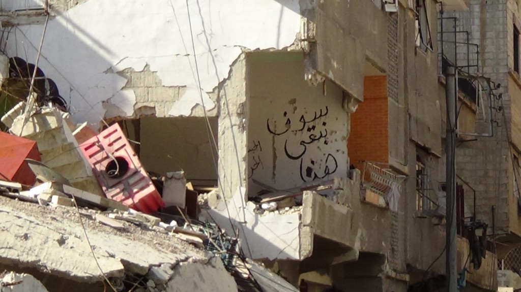 The words "We will stay here" are written on the wall of one of the destroyed buildings in Seil, along with a tribute to the Free Syrian Army. Photography by Razan Zeitouneh