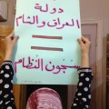 Suad holds up a placard that says "ISIS prisons= regime prisons." Photography by Zaina Erhaim.