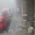 Residents in the Mashhad neighbourhood seek shelter in the doorways of buildings among billowing smoke from a recently dropped artillery shell. The shells are being fired from the “Artillery School” in the Rawasimah neighbourhood, headquarters of Air Force intelligence. The regime has not tried to infiltrate the Salah al-Din neighbourhood but has instead indiscriminately shelled it. October 10, 2013.