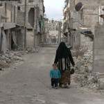 أمرأة تمشي مع طفلها في حارة مهدمة في السكري