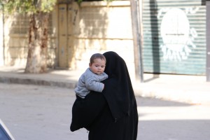 أمرأة تحمل رضيعها وتمشي في حي الزبدية. تصوير حسام كويفاتية